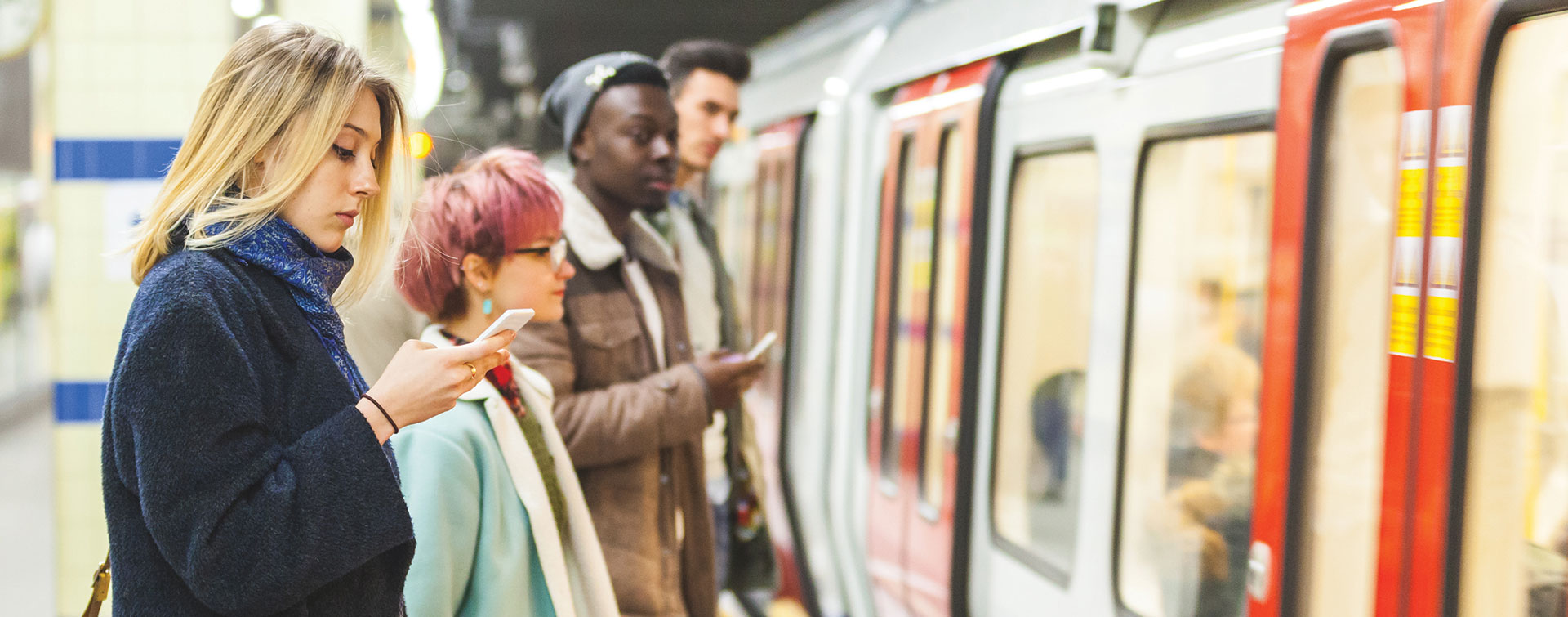 People waiting for the subway to arrive while they check their phones.